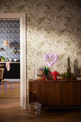 A room with a wooden cabinet against a patterned wallpaper, featuring decorative items and a view into another room.