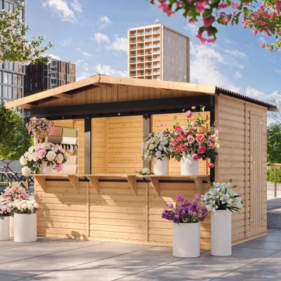 A wooden market stall decorated with various flower arrangements, set against an urban backdrop with buildings and a blue sky.