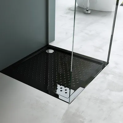 A close-up view of a modern black shower tray with a textured surface and a silver drain cover, set within a contemporary bathroom.