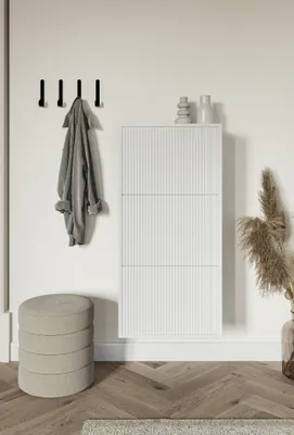 A minimalist entryway with a white shoe cabinet, a coat hanging on hooks, and a round ottoman.