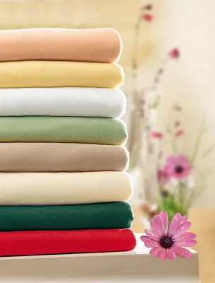 A stack of folded fabric sheets in various colors, with a pink flower in the foreground and blurred floral elements in the background.