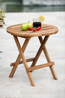 A round wooden table with a drink and fruit on it, set outdoors.