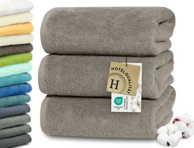 A stack of three brown towels with a tag attached to the middle towel. A stack of colorful towels is visible on the left side of the image.