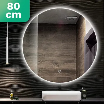 A round LED illuminated mirror is shown in a modern bathroom setting, reflecting the tiled wall and a door. A white sink is visible below the mirror.