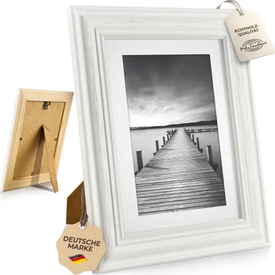 A white vintage-style picture frame with a black and white photo of a pier on a lake.