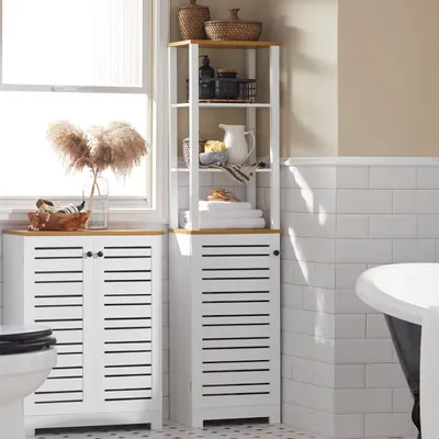A bathroom scene featuring two white storage cabinets with slatted doors and a tall white shelving unit with wooden accents, placed next to a toilet and a bathtub.