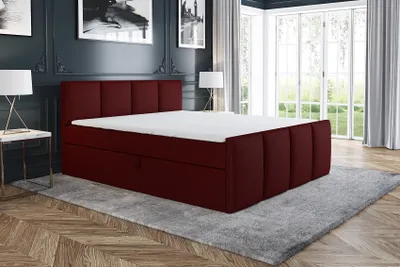 A bedroom scene with a dark red boxspring bed as the main focus, placed on a gray rug.