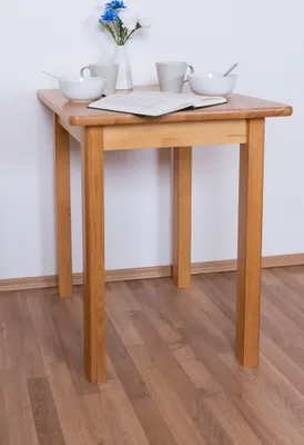 A small wooden table set for breakfast with two bowls of cereal, two mugs, a vase of flowers, and an open book.