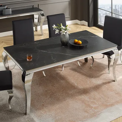 A dining room scene featuring a black marble-effect dining table with chrome legs, surrounded by black chairs. A vase with flowers and a bowl with fruit are on the table.