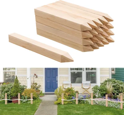 A stack of wooden stakes with one stake in the foreground, and a garden scene with a house in the background.