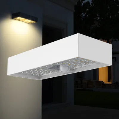 A modern white outdoor wall light with a motion sensor is mounted on a building's exterior wall at night.