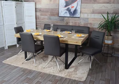 A dining set with chairs and a bench around a wooden table, placed on a rug in a room with a wood-paneled wall.