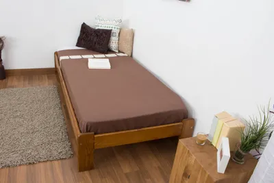 A single bed with brown bedding, placed in a room with wooden flooring and white walls.