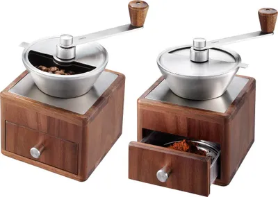 Two manual coffee grinders made of wood and stainless steel are shown against a white background. One grinder is shown with whole beans in the hopper, and the other is shown with ground coffee in the drawer.