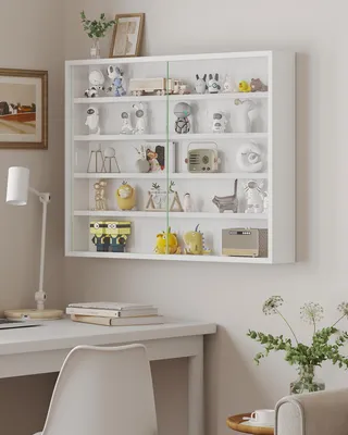 A white wall-mounted display cabinet filled with various decorative items, placed above a white desk with a lamp and books.