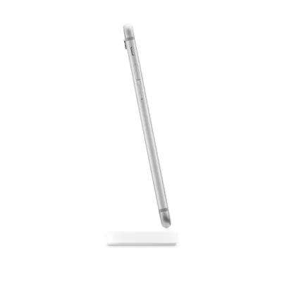 A silver iPhone is standing upright on a white dock station, viewed from the side against a white background.