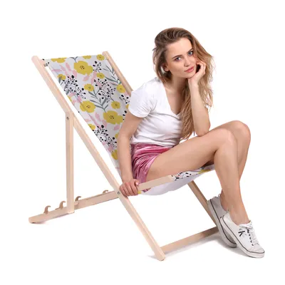 A young woman is sitting on a foldable wooden deck chair with a floral pattern.