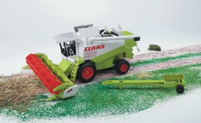 A toy combine harvester is shown on a diorama of a field with grass and dirt.