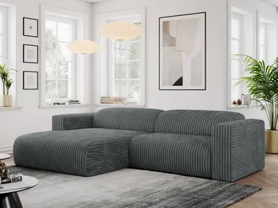 A modern living room with a dark gray corduroy sectional sofa as the main focus, placed on a rug in front of a window and a piece of abstract art.