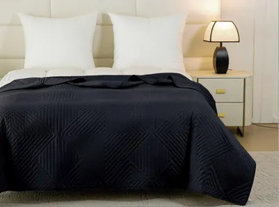 A dark navy blue quilted bedspread is draped over a bed with two white pillows. A bedside table with a lamp is visible to the right.