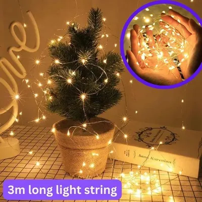 A small decorated Christmas tree with fairy lights, a book, and a neon sign in the background.
