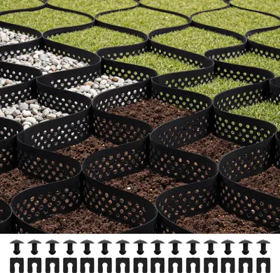 A close-up view of a black honeycomb grid system filled with gravel and soil, with green grass visible in the background. The grid is designed for ground stabilization.