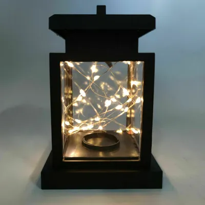 A black lantern with fairy lights inside, set against a light gray background.