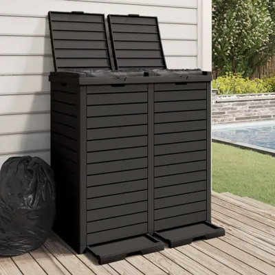 A dark gray outdoor trash can with two compartments, placed on a wooden deck next to a swimming pool.