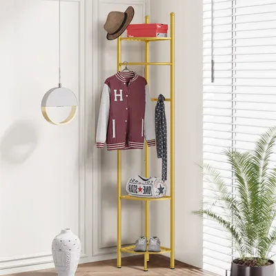 A gold metal corner coat rack with shelves, displaying clothing, a hat, a bag, and shoes.