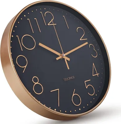 A close-up, angled view of a modern wall clock with a black face and gold numerals and hands, set against a white background.