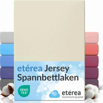 A cream-colored fitted sheet is shown standing upright, with stacks of fitted sheets in various colors visible on the left and right sides. Cotton bolls are placed at the bottom left, and a logo and text are present on a blue band across the lower part of 