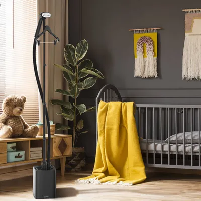 A nursery room with a teddy bear, a garment steamer, a crib with a yellow blanket, and wall decor.