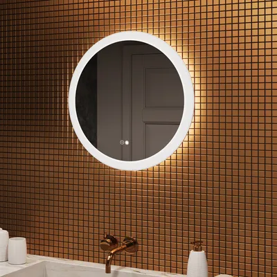 A round mirror with integrated LED lighting is mounted on a wall covered in small, square, copper-colored tiles. Below the mirror, a marble countertop is visible with a copper faucet and a white soap dispenser.