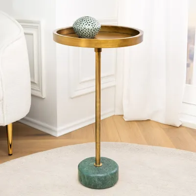 A decorative spherical object rests on a small round table with a brass stem and a green marble base, next to a white armchair and by a window with white curtains.