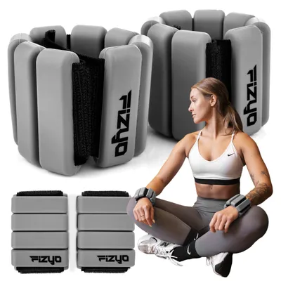 A woman is sitting on the floor wearing ankle weights, with other ankle weights stacked in the foreground and background.