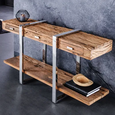 A wooden console table with metal legs and drawers, placed against a stone wall.