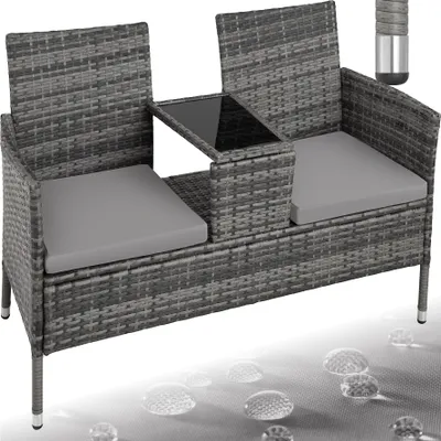 A gray rattan garden bench with a small table in the middle, shown against a white background with water droplets on the surface below.