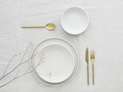 A minimalist table setting with white plates and gold cutlery.