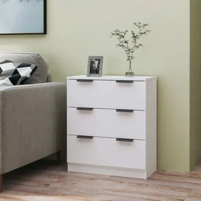 A white three-drawer dresser is placed next to a gray sofa in a room with light green walls and a wooden floor.