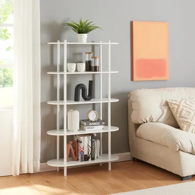 A white bookshelf filled with decorative items and books, placed in a living room next to a sofa and a window.
