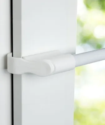A close-up view of a white tension rod bracket attached to a white frame, with a blurred green and yellow background suggesting an outdoor scene.