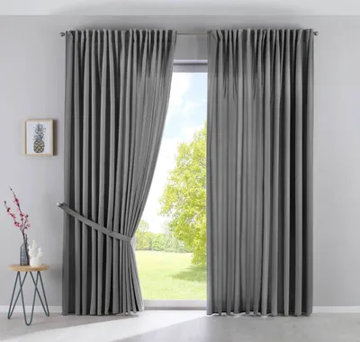 A pair of gray curtains are shown, one partially drawn back, revealing a view of trees and sky outside a window.