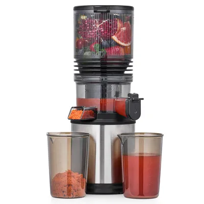 A slow juicer with fruits in the top chamber and juice in a beaker.
