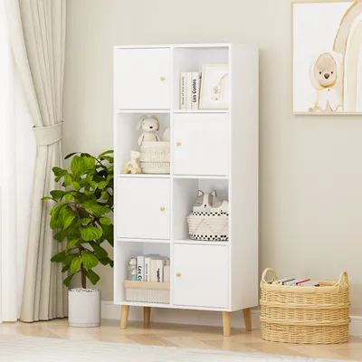 A white bookshelf with wooden legs is shown in a room with a plant and curtains.