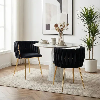 A dining set with two black velvet chairs and a marble-top table, set in a well-lit room with a large abstract painting and a potted plant.