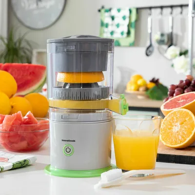 A kitchen counter with a juicer, fruits, and a glass of juice.
