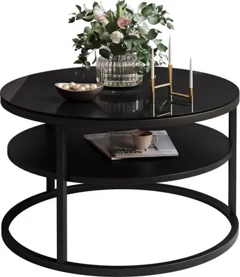 A round coffee table with a glass top and a lower shelf, decorated with a vase of flowers, a bowl of decorative items, and two candles in a holder.