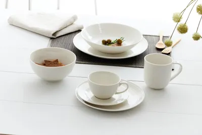 A white ceramic coffee and dinnerware set arranged on a white table.