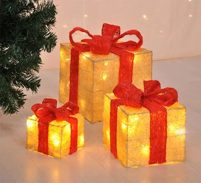 Three illuminated gift boxes with red bows are arranged on a floor next to a Christmas tree.