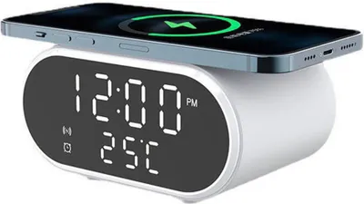 A white digital alarm clock with a wireless charging pad on top, charging a smartphone. The clock displays the time and temperature.